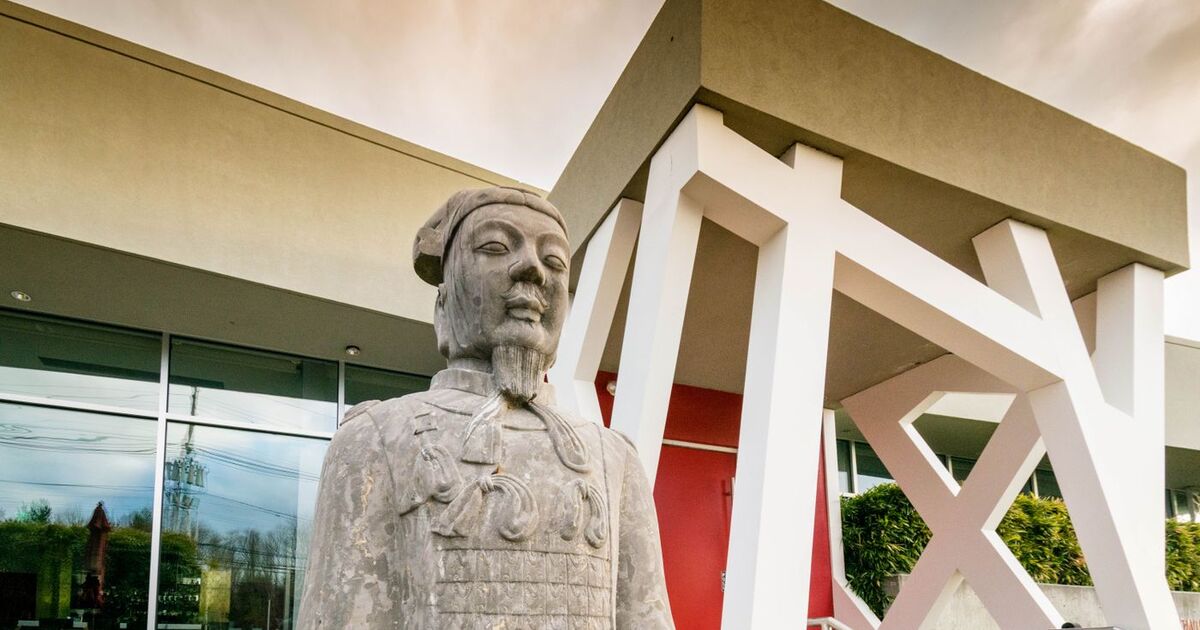Modern architectural elements blend with a terracotta warrior statue in an outdoor urban setting.