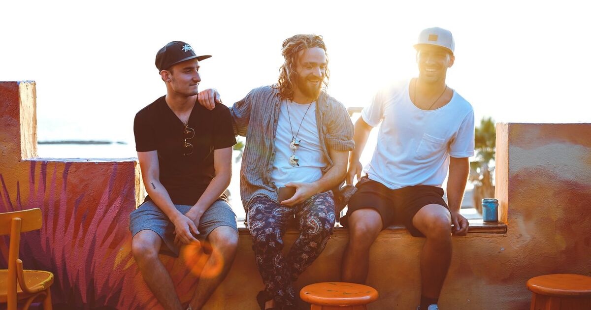 Three friends relax on a Tel Aviv rooftop, soaking up a vibrant sunset atmosphere.