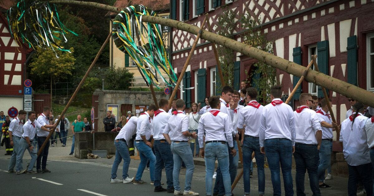 Men in traditional attire participate in a Bavarian maypole setup in Großhabersdorf, Germany, showcasing cultural heritage.