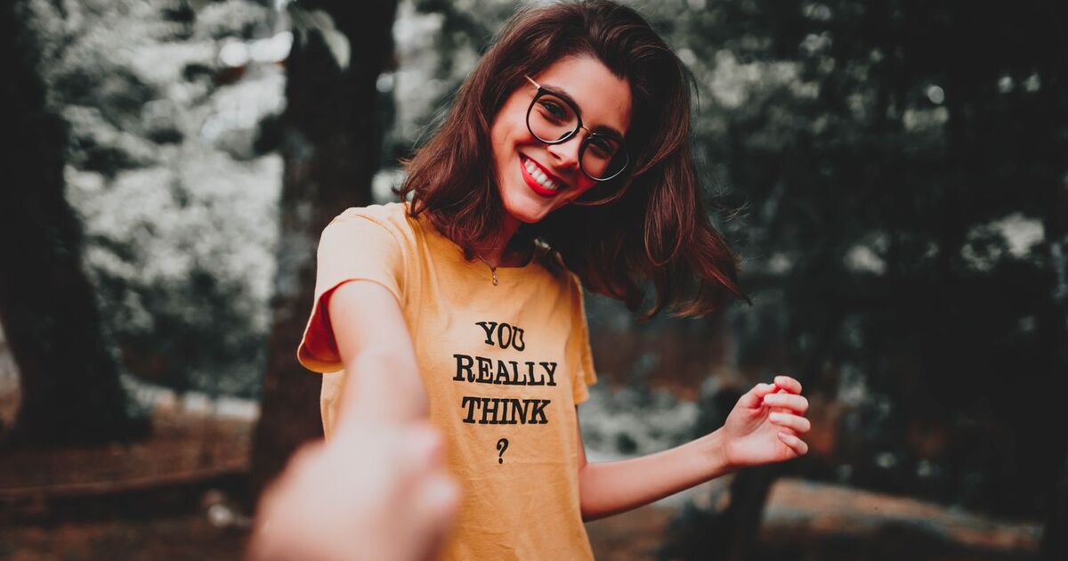Cheerful woman in glasses holding hands outdoors, wearing a text t-shirt.
