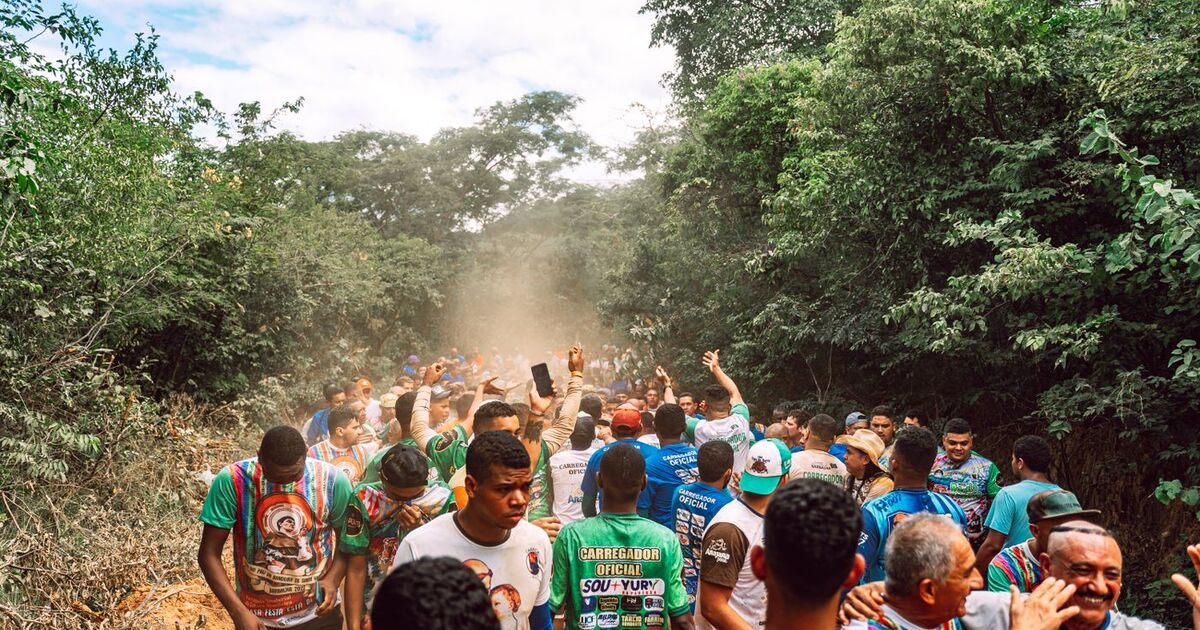 A vibrant crowd walking on a dusty road through the forest during a festival in Barbalha, Brazil.