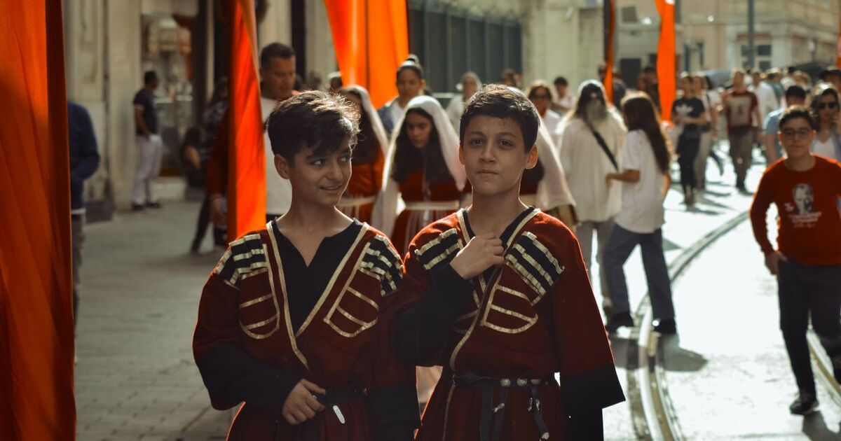 Boys in traditional costumes stroll along bustling Istanbul street, capturing cultural essence.