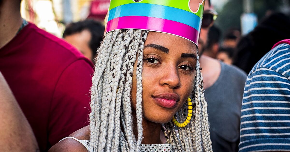 Portrait of a woman with braided hair and colorful crown at a street celebration in São Paulo, Brazil.