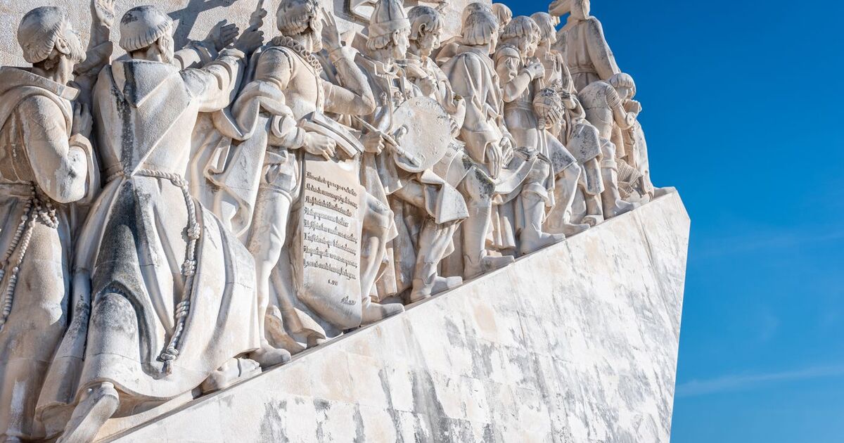 Stone sculptures of explorers on Monument to the Discoveries in Lisbon against a blue sky.