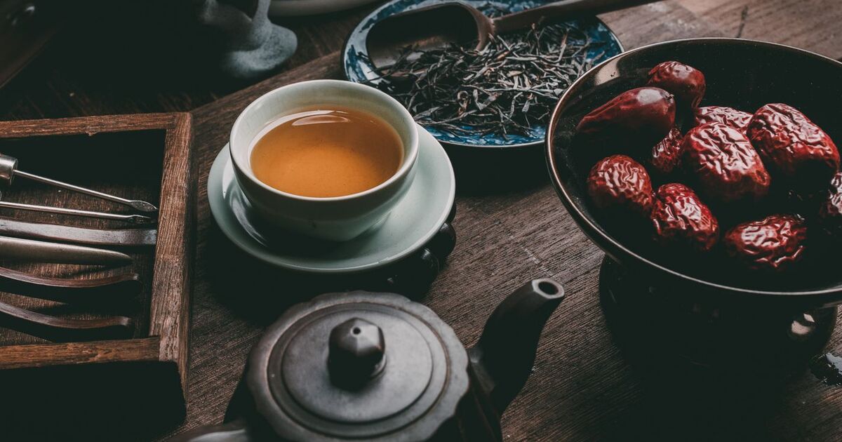 A rustic tea setup featuring a cup of tea, dried red dates, and tea leaves on a wooden table.