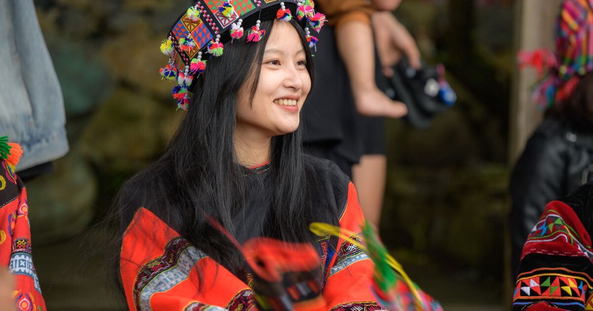 Woman wearing vibrant traditional attire and headdress, smiling joyfully.