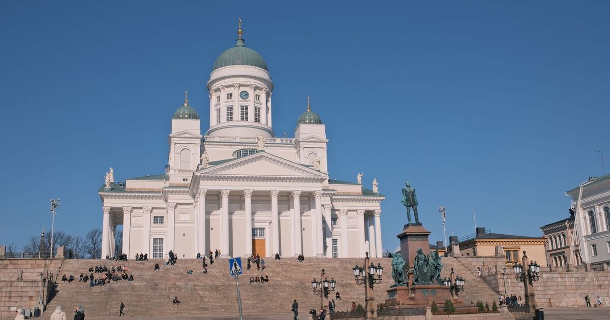 View of Helsinki Cathedral with surrounding architecture and statue under a clear blue sky.