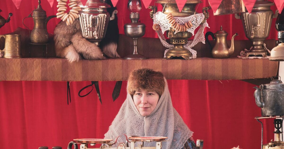 Woman in traditional attire with samovars at Russian market in winter.