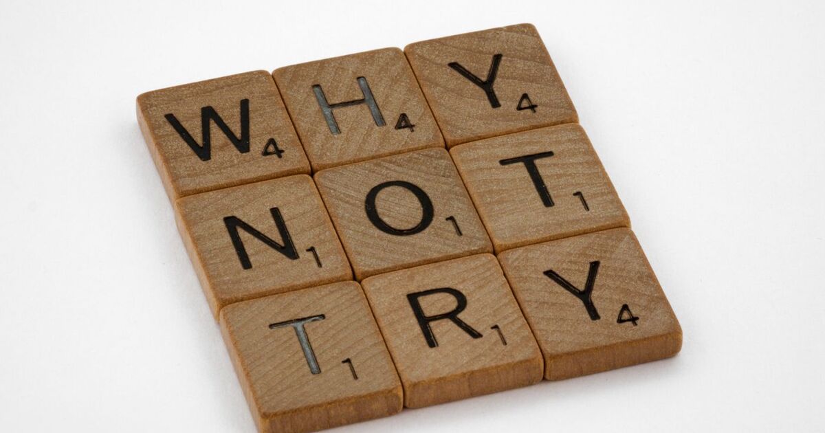 Wooden Scrabble tiles on a white background spelling the phrase 'Why Not Try'.